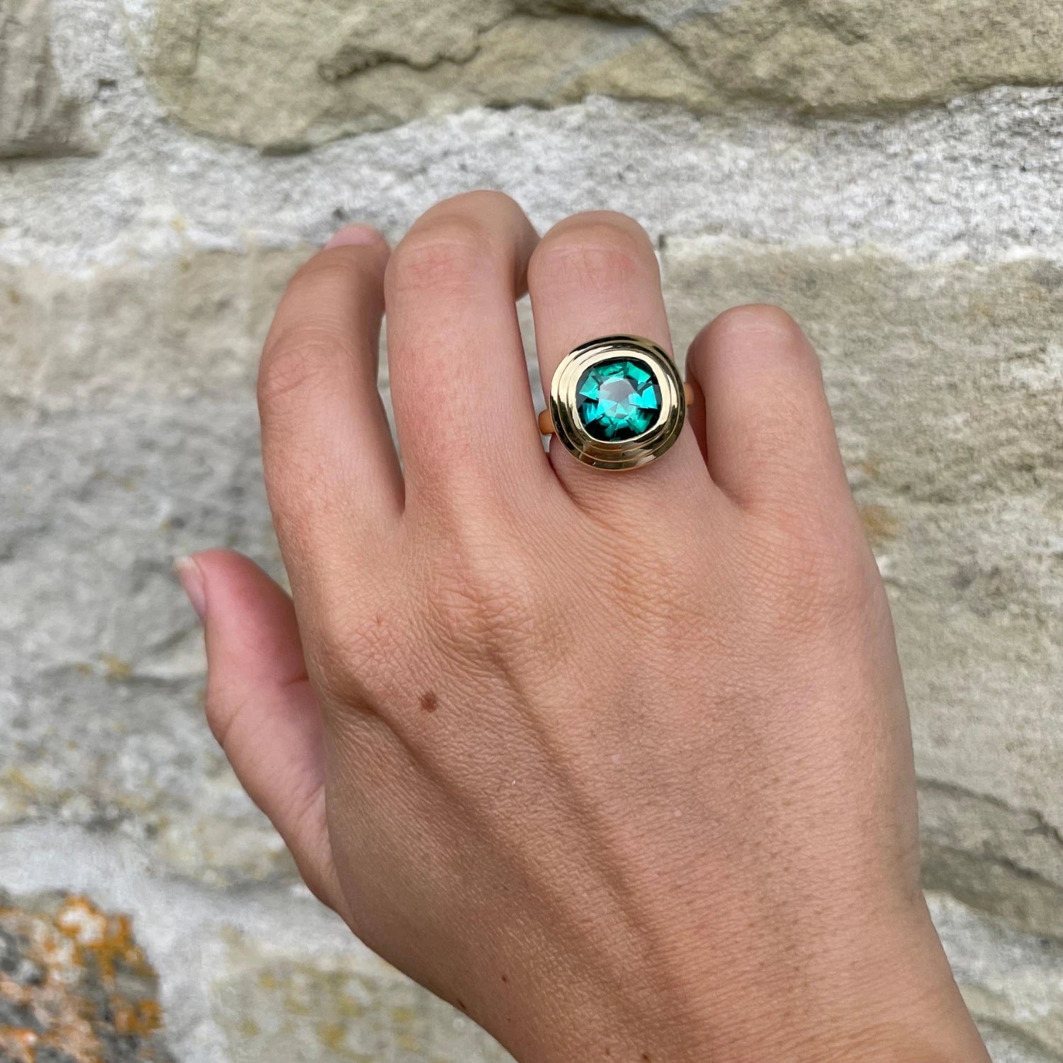 Hand wearing Athena 4.56ct green tourmaline ring in 18k yellow gold with cushion-cut forest green tourmaline