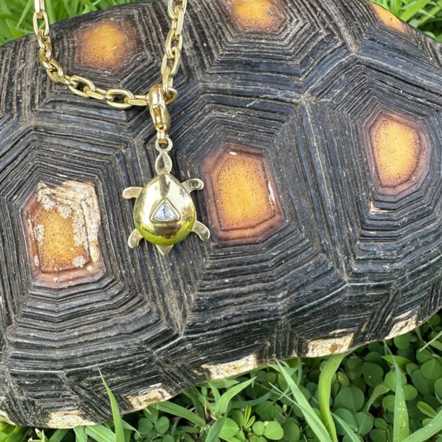 Lifestyle image of Atlantis dancing turtle diamond charm in solid 18k yellow gold with trillion-cut diamond attached to a necklace chain