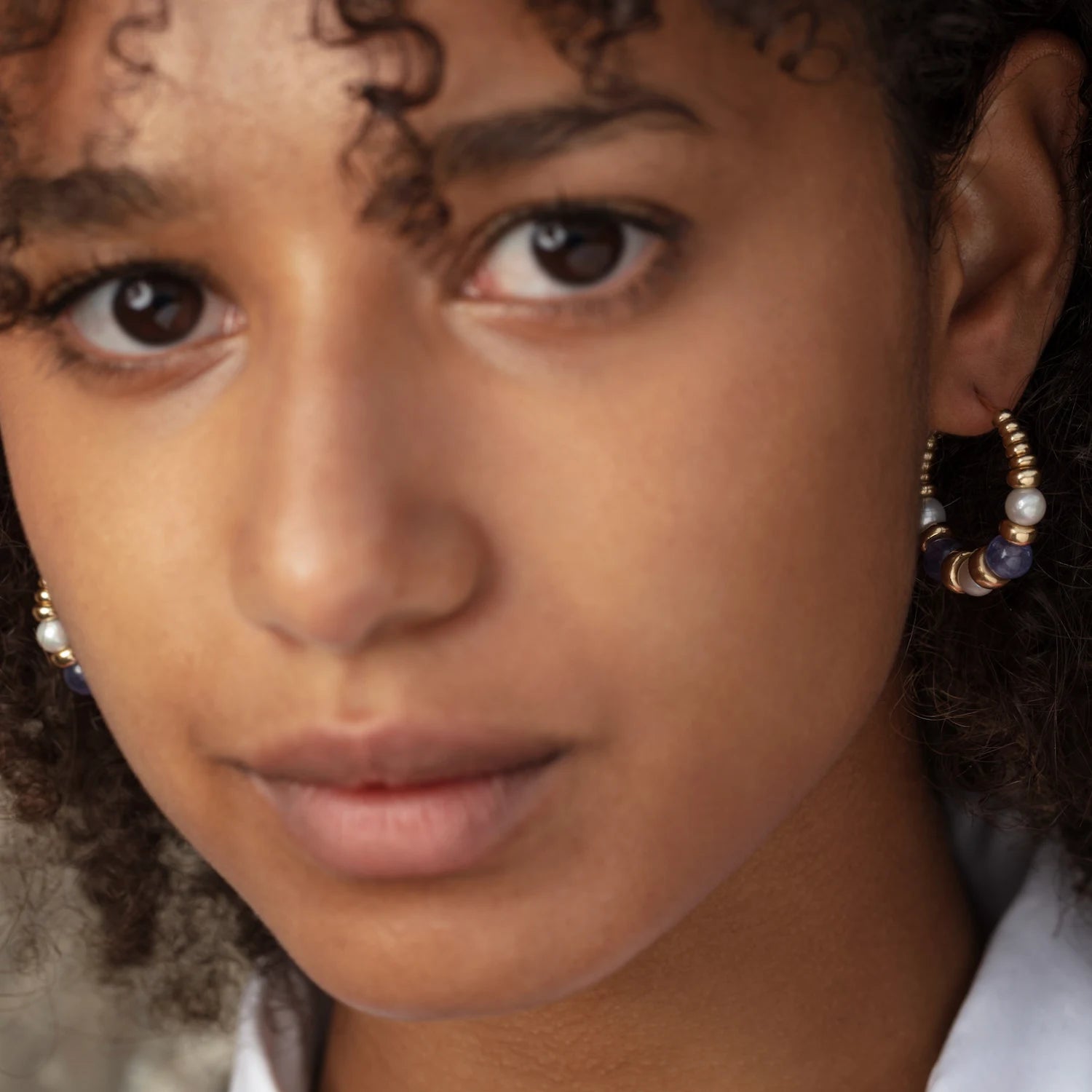 Model wearing tanzanite and pearl hoop earrings in 18k yellow gold with 30mm hoops, purple beads, and white pearls