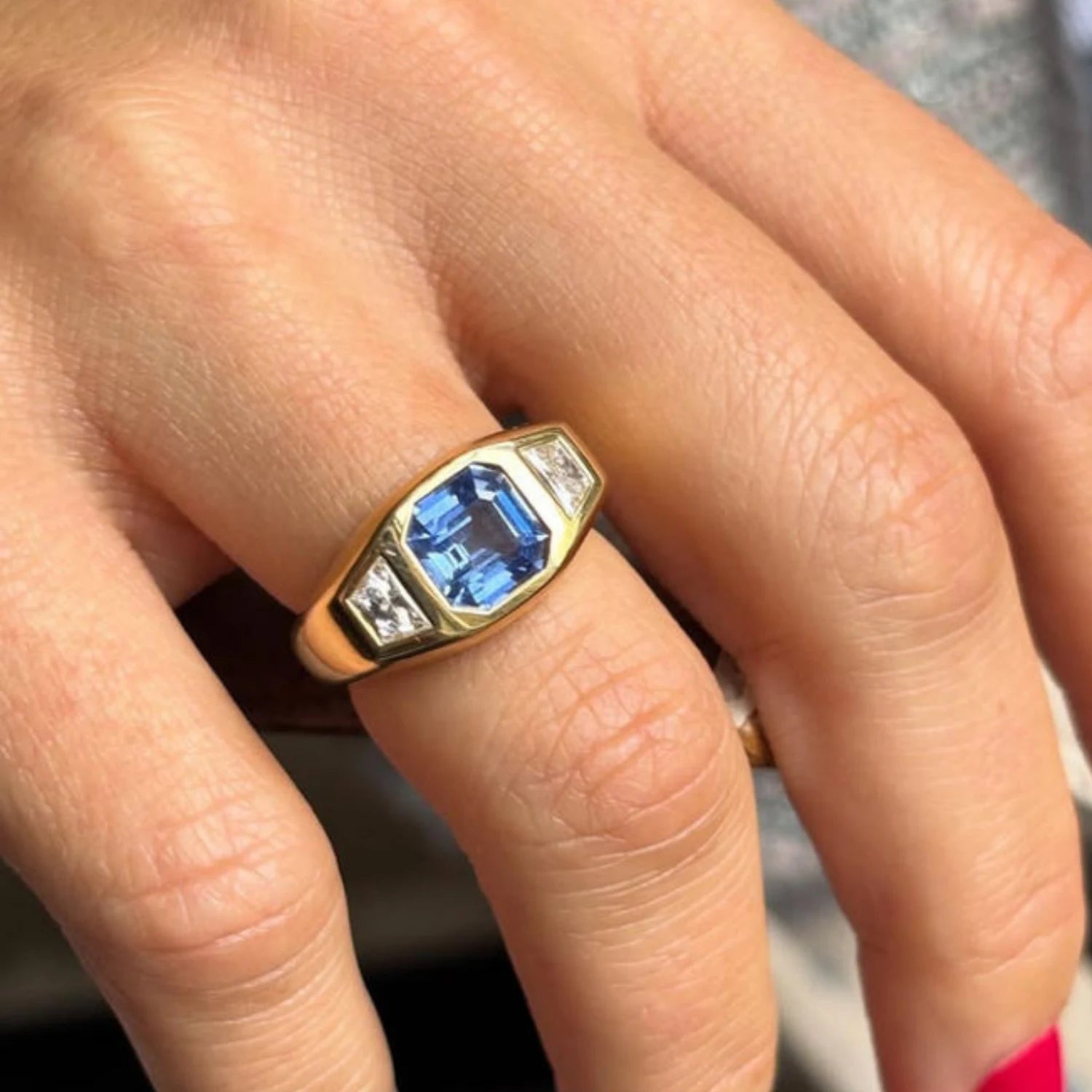 Hand wearing octagon sapphire and diamond ring in 18k yellow gold with 2.54ct blue sapphire and trapezoid-cut diamonds