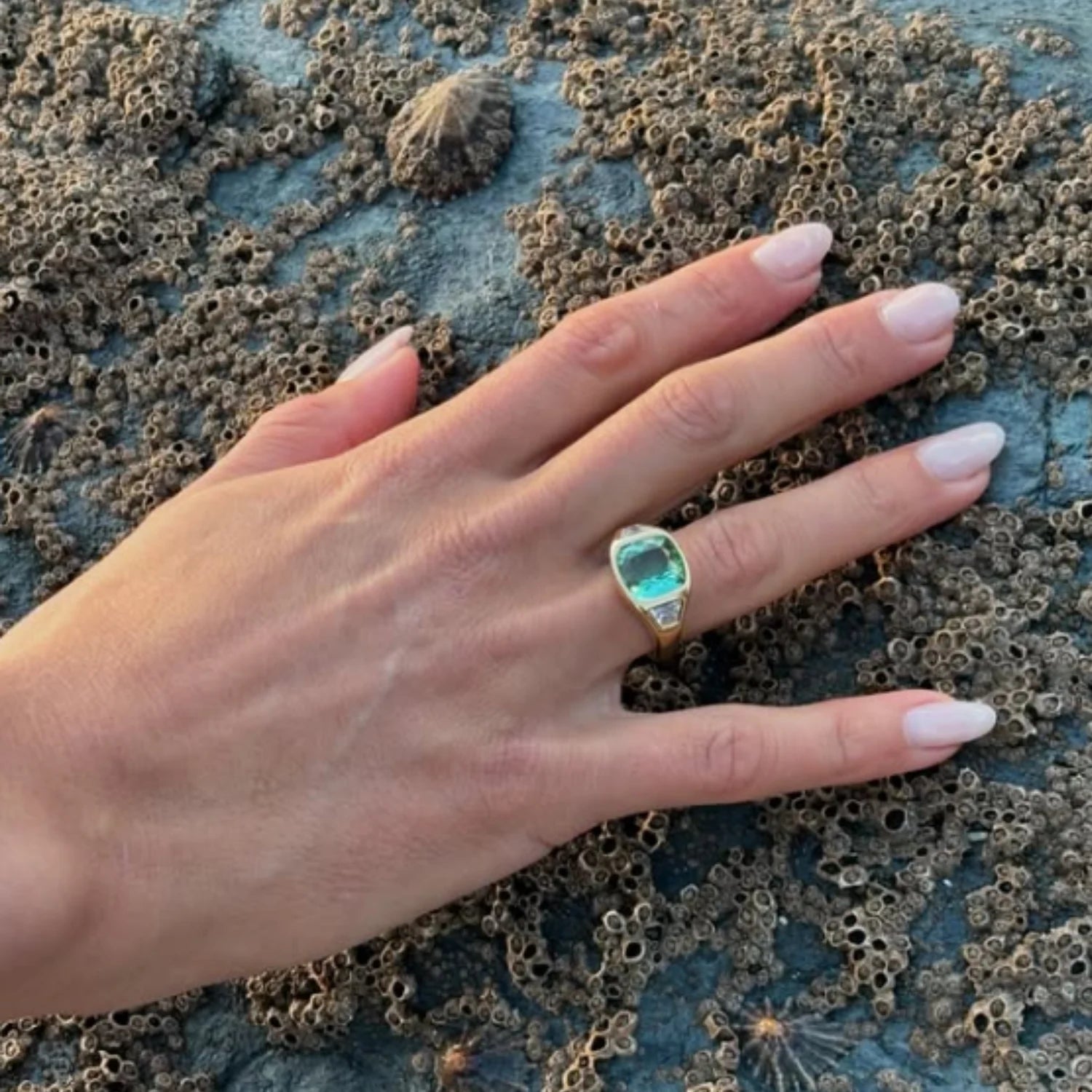 Hand wearing green tourmaline and diamond ring in 18k yellow gold with 5ct cushion-cut center stone and trapezoid-cut diamonds