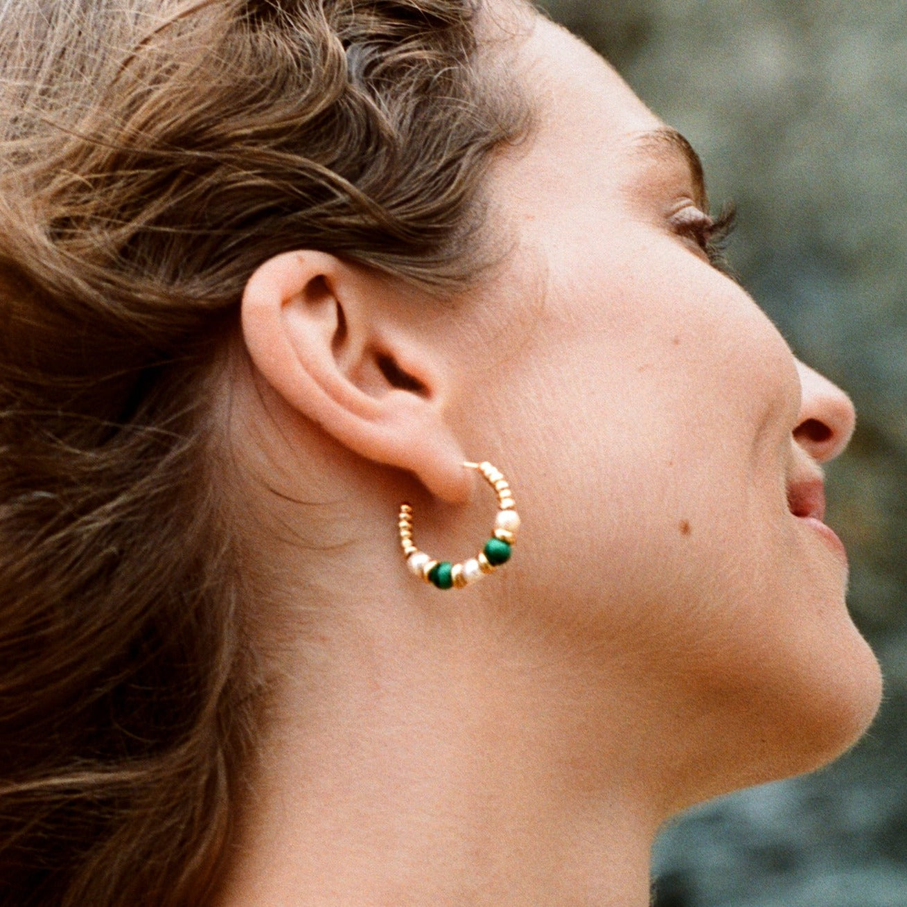 Model wearing 25mm Mermaid collection hoop earrings in 18k yellow gold with malachite and white pearls