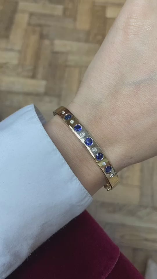 Lifestyle shot of 18k yellow gold hinged bangle featuring five blue sapphires and five diamonds, highlighting sparkling elegance for bridal or everyday wear.