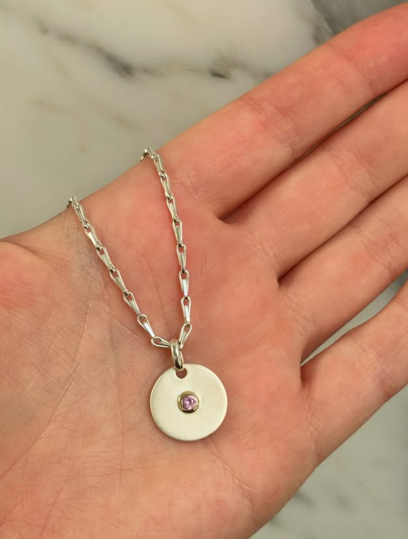 Close-up of Limited Edition Pink Sapphire Silver Disc Pendant with engraved kiss and pink sapphire gemstone