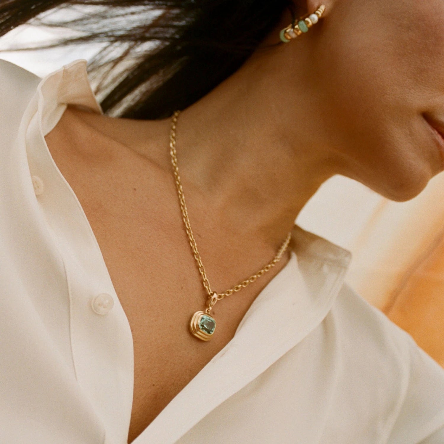 Model wearing Athena blue tourmaline pendant necklace in 18k yellow gold with cushion-cut blue tourmaline