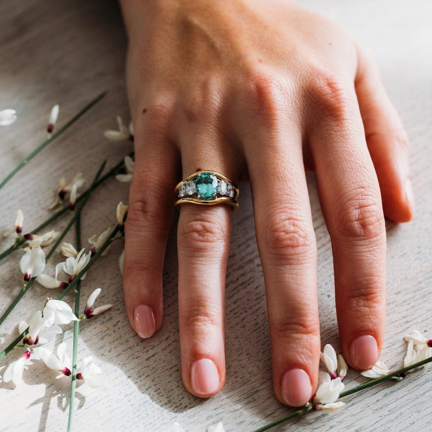 Hand wearing Atlantis ring showing green tourmaline center stone with four oval-cut white diamonds in 18k yellow gold
