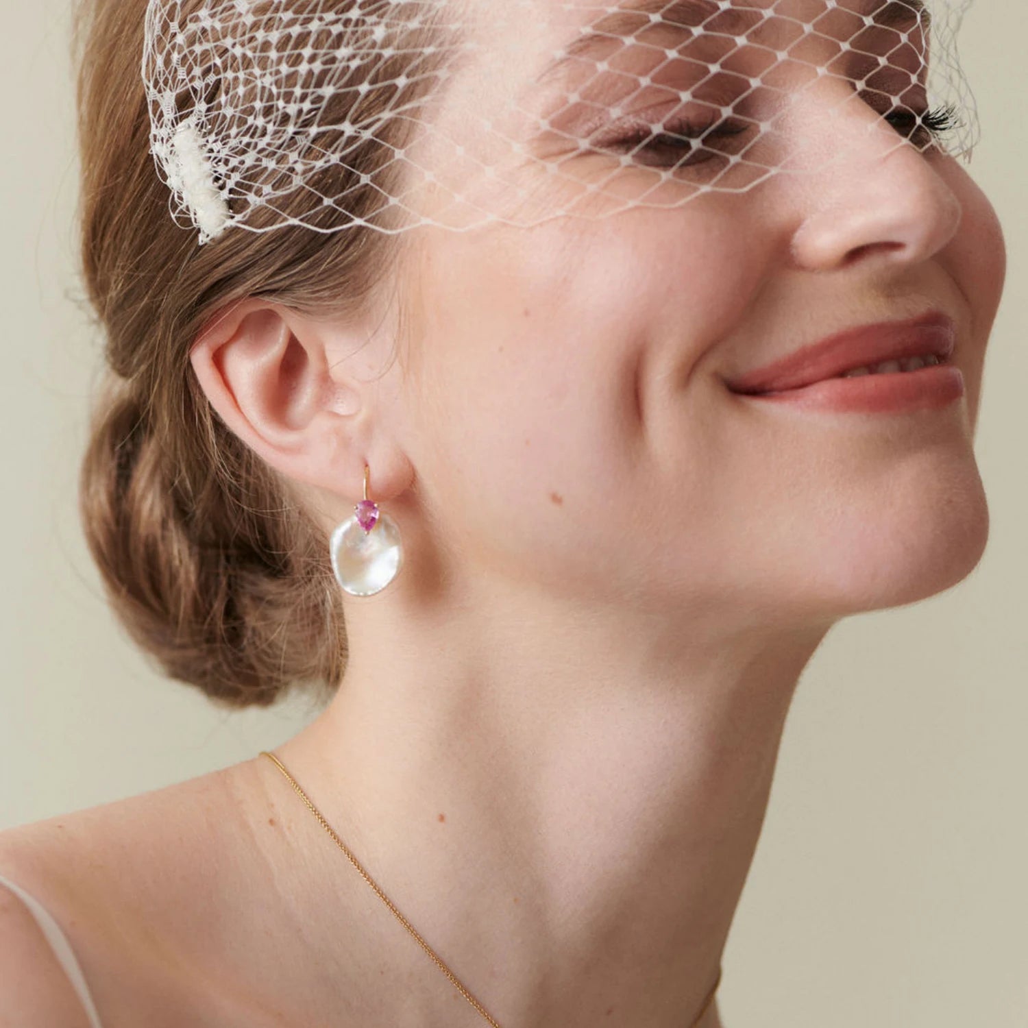 Model wearing Atlantis 18k yellow gold earrings with pink pear-shaped sapphires and unique white Keshi pearls