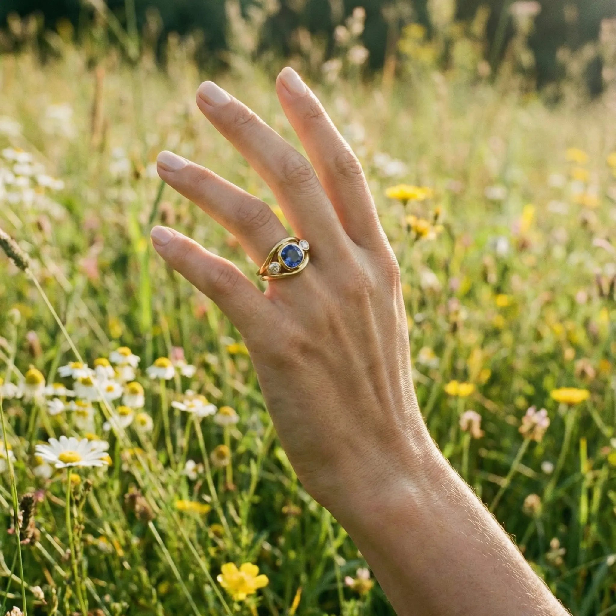 Blue sapphire and diamond Atlantis ring on model’s hand, showing mermaid-inspired double curved band