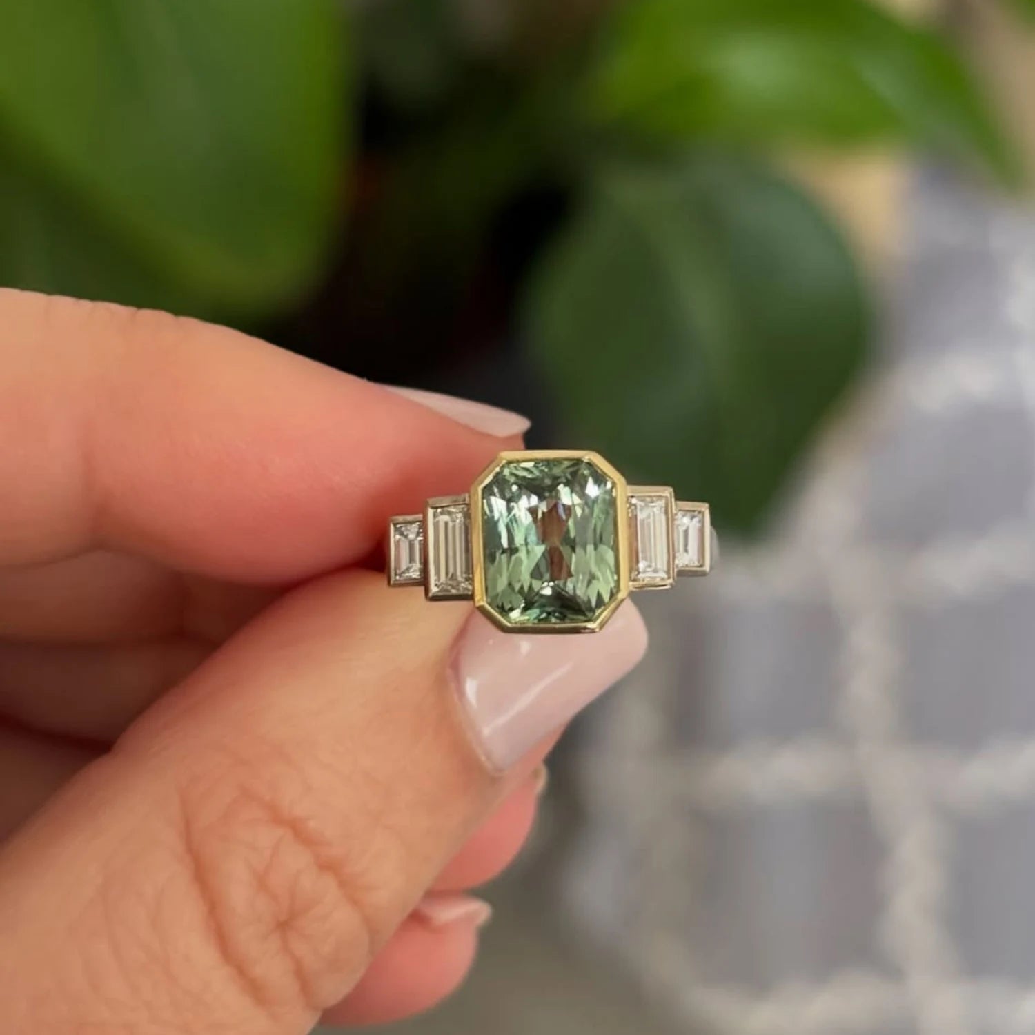 Close-up of emerald-cut green sapphire ring showing deep green center stone and baguette-cut white diamonds in 18k yellow gold