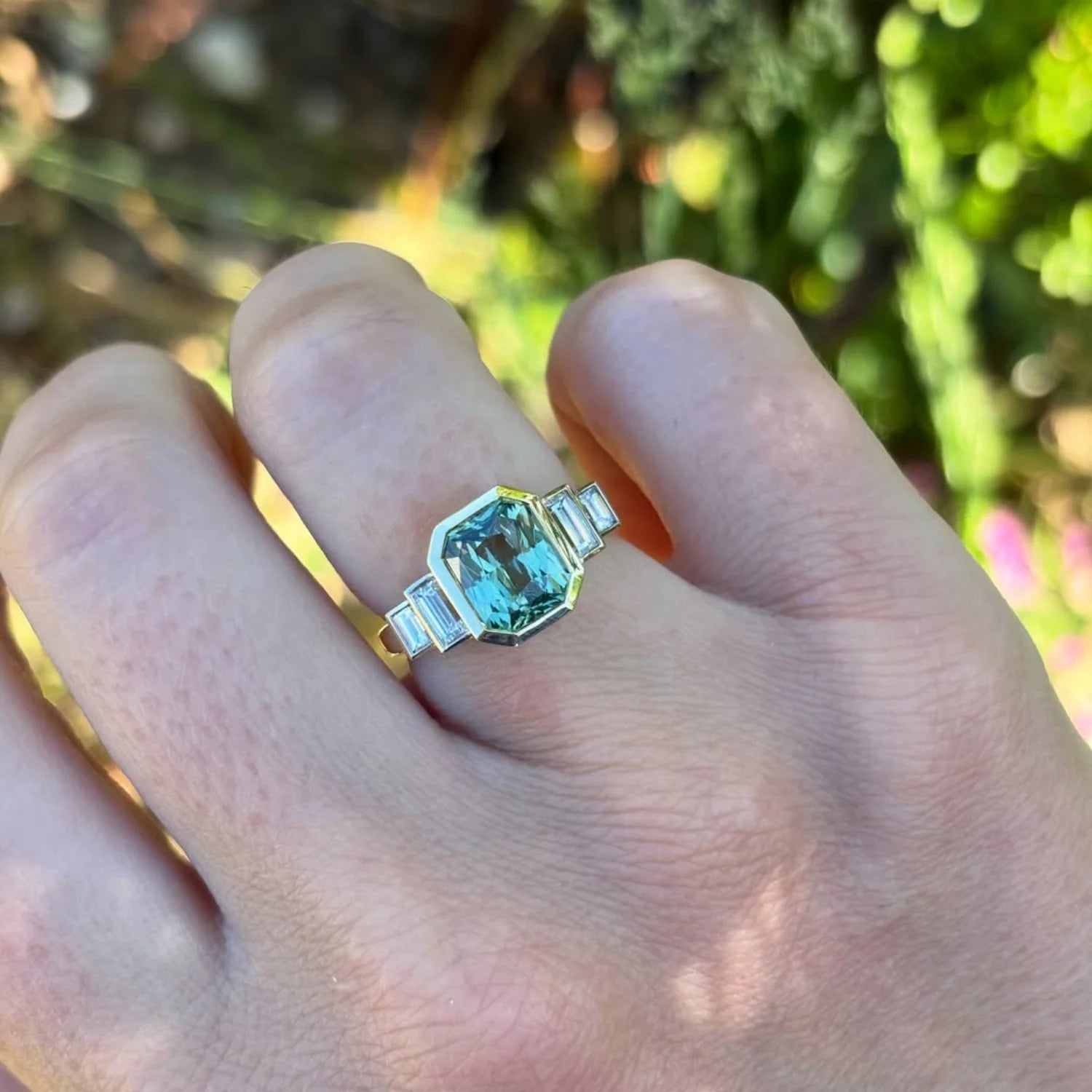 Lifestyle image of emerald-cut green sapphire and diamond ring in 18k yellow gold, elegant bridal jewelry design