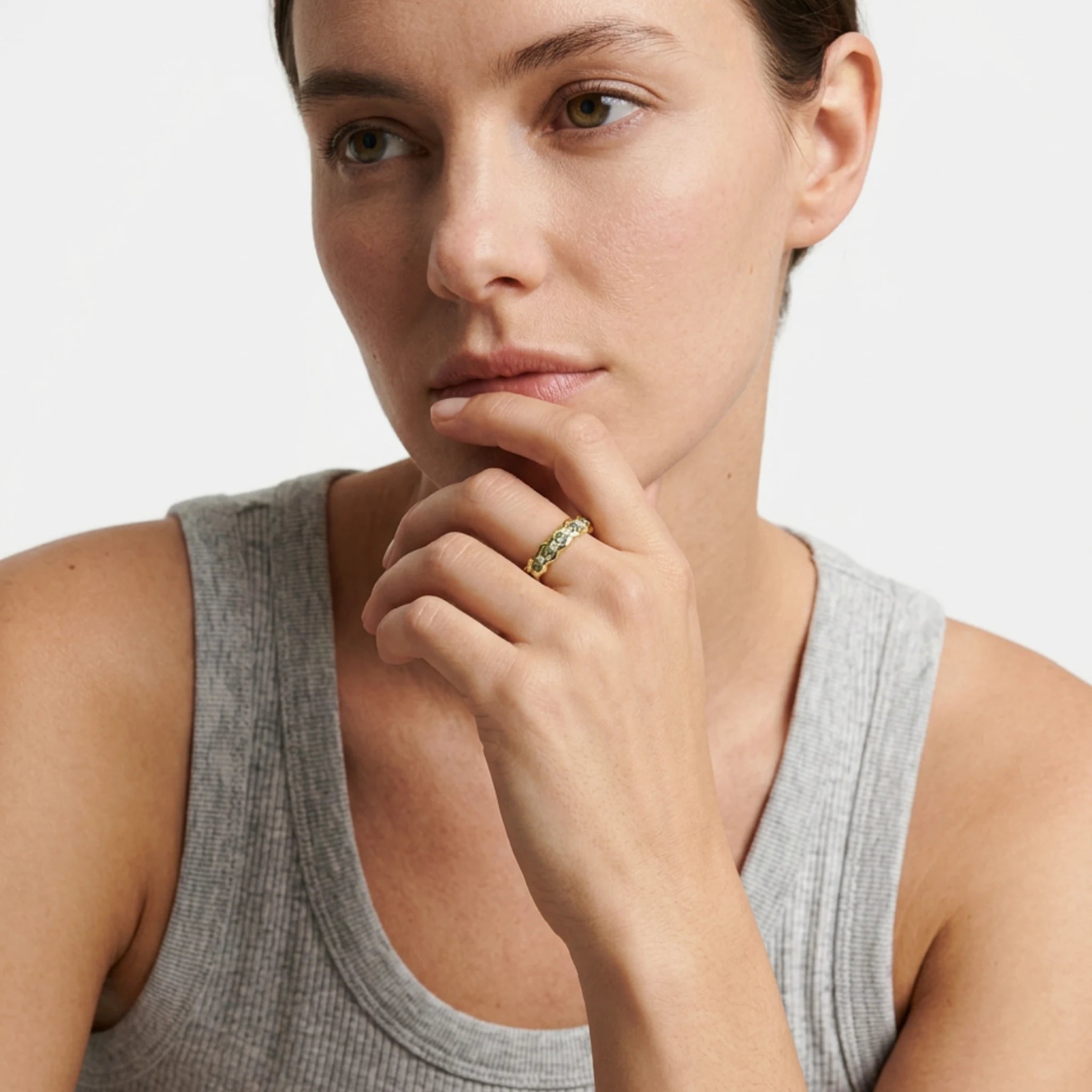 Model wearing green sapphire and diamond eternity ring in solid 18k yellow gold with wavy band, vivid green sapphires and round-cut white diamonds