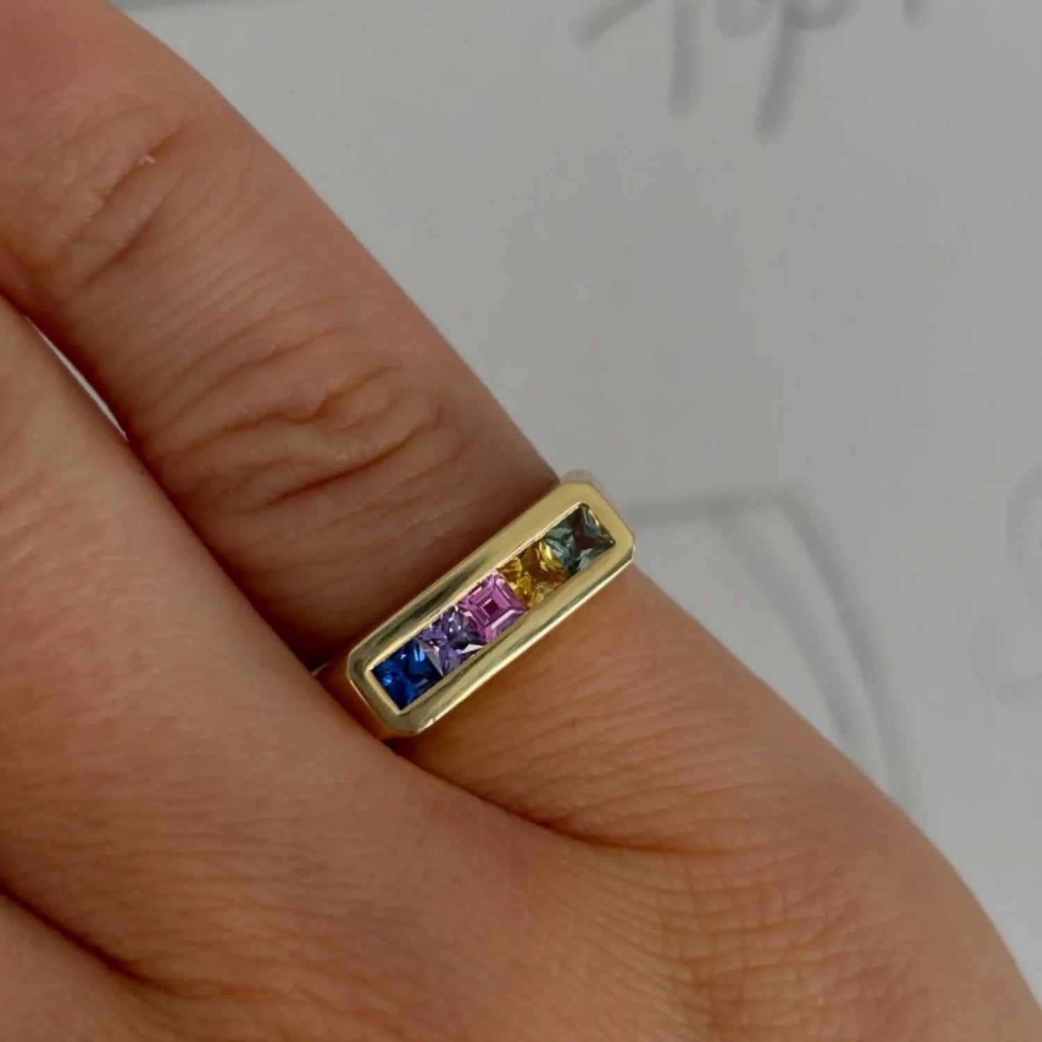 Hand model wearing Ley Lines Rainbow Sapphire Pinky Ring, 18k gold with five princess-cut rainbow sapphires, colorful stackable style
