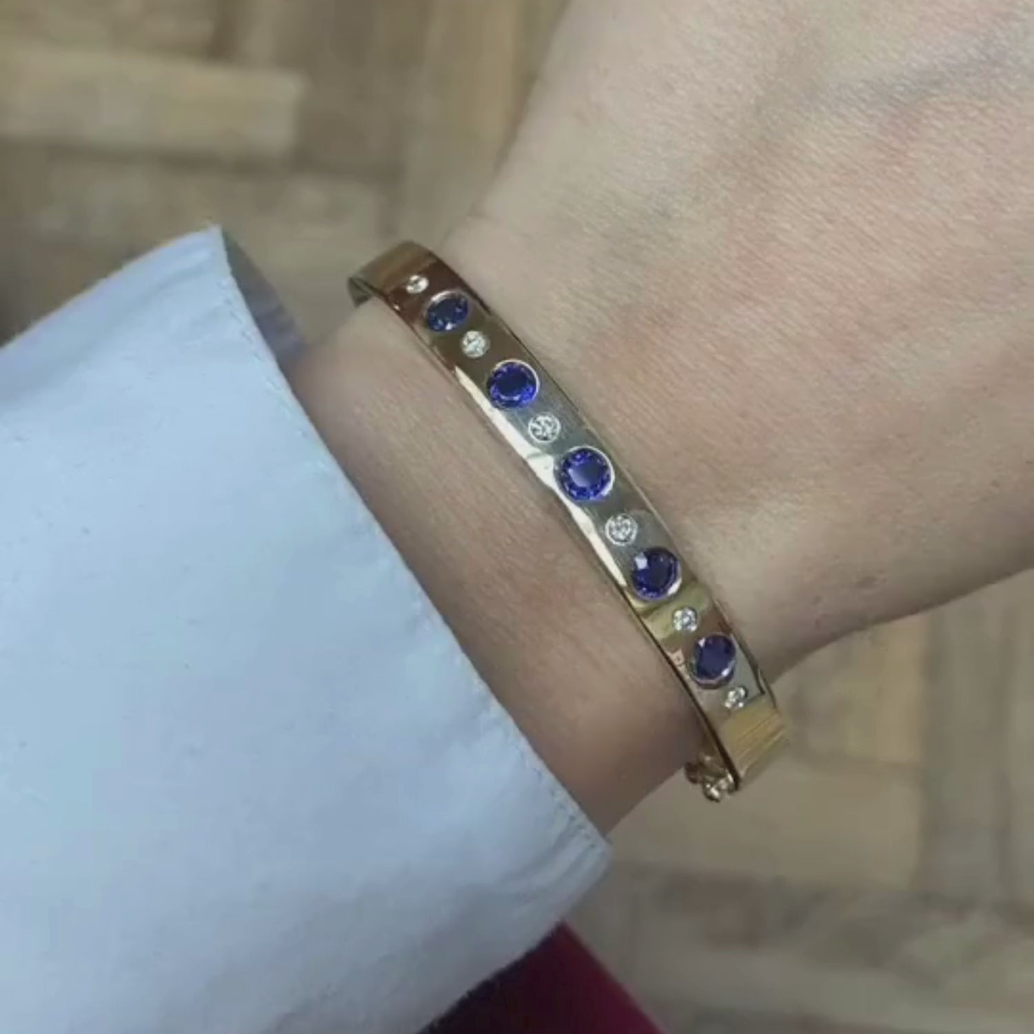 Close-up video of sapphire and diamond bracelet showing alternating blue sapphires and white diamonds in 18k yellow gold hinged bangle